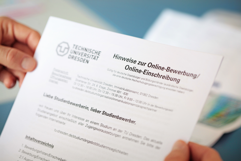 The photo shows the hands of one person. In these she holds a form with the inscription: "Hinweise zur Online-Bewerbung/Online-Einschreibung"