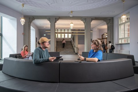 zwei Personen sitzen auf einem Sofa in einem Foyer und lächeln sich an
