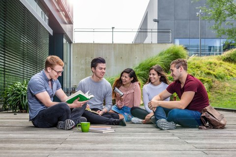 Photo: Five happy students sitting on a wooden terrace of the Andreas Pfitzmann Building