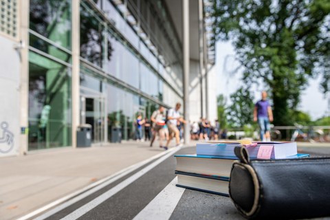 Das Foto zeigt das Hörsaalzentrum der TU Dresden. Im Fokus stehen zwei Bücher und eine Federmappe. Sie liegen auf der Treppe vor dem Hörsaalzentrum