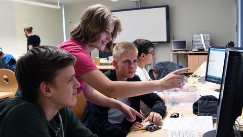 Schülerinnen und Schüler diskutieren vor einem PC.