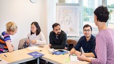 Seminar mit zwei Studentinnen und zwei Studenten die am Tisch sitzen und eine Referentin