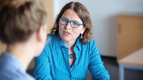 The photo shows a conversation between two people during a student counselling session. The student counsellor is looking towards the camera, the other person can be seen from behind.