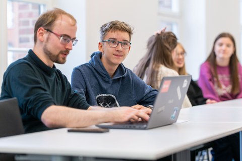 Teilnehmer schreibt am Laptop mit, ein weiterer Teilnehmer hört zu