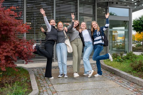 Es sind fünf Teilnehmer:innen der Herbstuniversität zu sehen, die in die Luft springen und fröhlich schauen. Sie stehen vor dem Gebäude der AOK PLUS, einem Projektpartner der Herbstuniversität.