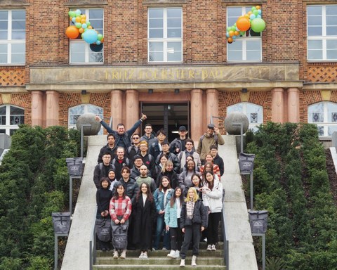 Foto einer Gruppe von lächelnden Studierenden, die auf einer Treppe vor einem Gebäude postiert sind