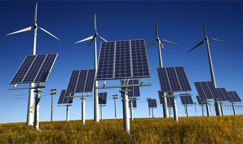 Das Foto zeigt im Vordergrund mehrere Solaranlagen und im Hintergrund mehrere Windräder.