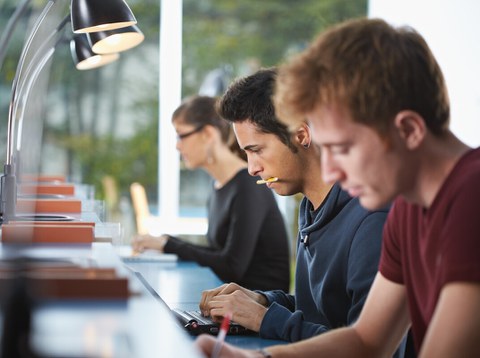 Foto von drei Studenten, die in der Bibliothek nebeneinander sitzen und für sich lernen.