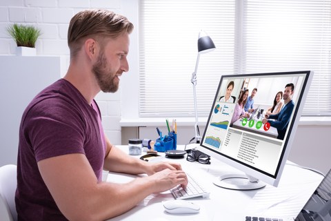 Foto: Mann sitzt am Schreibtisch vor seinem PC-Monitor und schaut in eine Videokonferenz