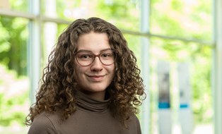 Portraitfoto: freundlich lächelnd, dunkle Brille, lange lockige Haare