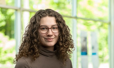 Portraitfoto: freundlich lächelnd, dunkle Brille, lange lockige Haare