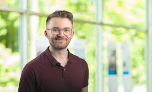 Tobias Dittrich hat kurze dunkelblonde Haare, eine Brille und trägt ein dunkelrotes Poloshirt.