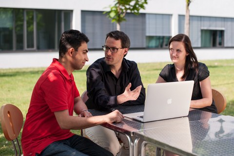 Drei junge Menschen im Gespräch vor einem Laptop im Freien