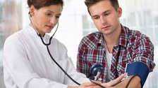 The photo shows a doctor taking a young man's blood pressure.