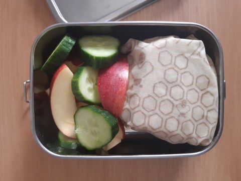 Lunchbox with sandwich wrap up in beewax wraps ad slices of apples and cucumber