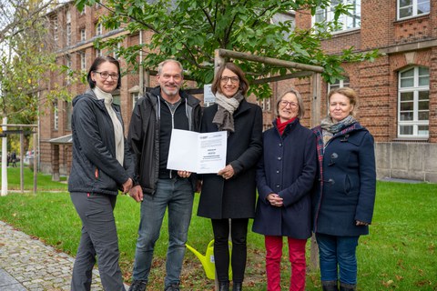 fünf Personen stehen an einem Baum 