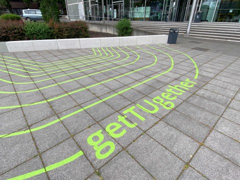 grün-gelbe Streifen als Markierung auf den Betonsteinen des Bodens im Außenbereich am Hörsaalzentrum, dazu gehört auch der Text getTUgether