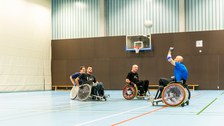 Foto mehrerer Männer in einer Turnhalle. Die Männer sitzen in Rollstühlen und spielen Rugby. 