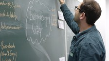 Foto eines Studenten, der an einer Tafel steht und diese beschriftet.