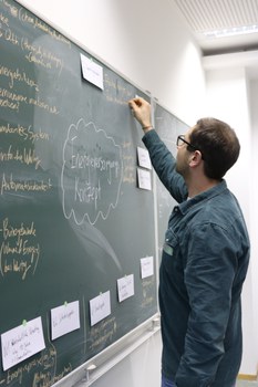Foto eines Studenten, der an einer Tafel steht und diese beschriftet.