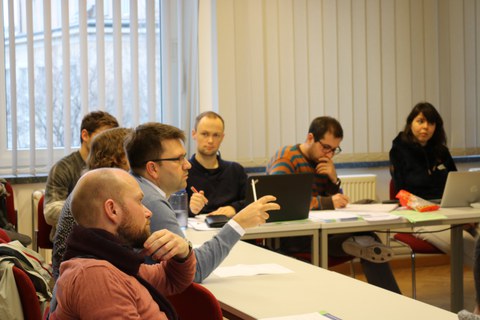 Foto der Profirunde. Die Profis sitzen in einer Reihe an einem Tisch und machen sich Notizen.