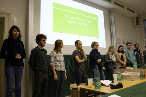 Foto von der Abschlusspräsentation. Eine Gruppe Studierende steht vor einer Leinwand und präsentiert.