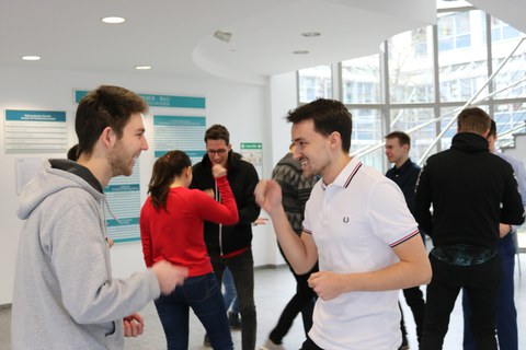 Foto von Studierenden bei einer Teammethode. Sie stehen paarweise zusammen und spielen Schere, Stein, Papier.