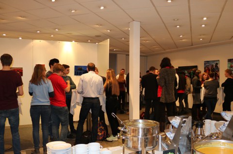 Foto des Get-together bei der Abschlussveranstaltung. Viele Personen stehen in einem Foyer und unterhalten sich. Im Vordergrund ist ein Buffet erkennbar.