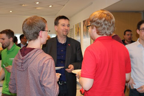 Foto des Get-together bei der Abschlussveranstaltung. Zwei Studenten unterhalten sich mit einem Industrievertreter.