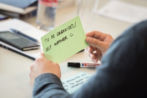 Ein Teilnehmer schreibt die Eigenschaften "to be organized" und "to be a self manager" auf eine Karte.