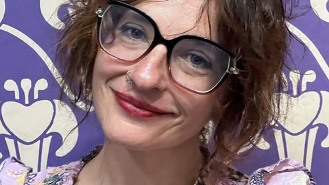 Prof. Orit Halpern in a flowery blouse in front of a expressionistic wall