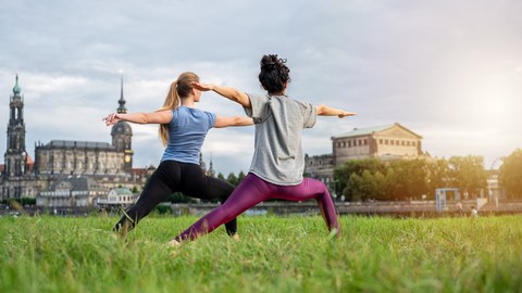 Zwei Frauen stehen in der Yogaposition "Krieger" am Elbufer