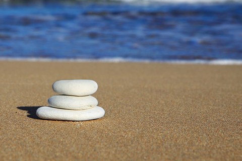 Drei flache, weiße Kieselsteine liegen gestapelt am Strand, im Hintergrund das Meer