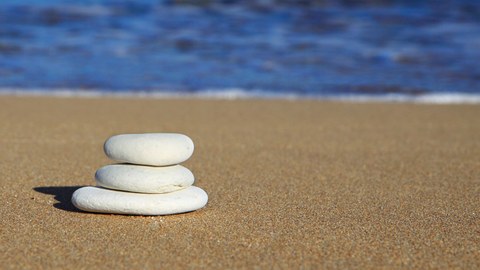 Drei flache, weiße Kieselsteine liegen gestapelt am Strand, im Hintergrund das Meer