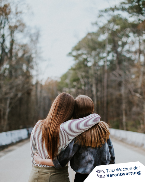 zwei junge Frauen stehen auf einer leeren Straße und nehmen sich in den Arm