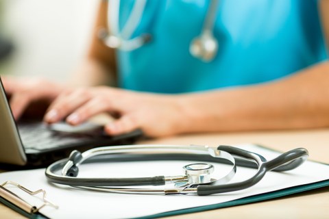 Stethoskop auf einem Tisch, im Hintergrund Person mit Arztkittel