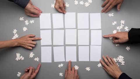 Foto von mehreren Händen, die gemeinsam ein Puzzle zusammenfügen. 