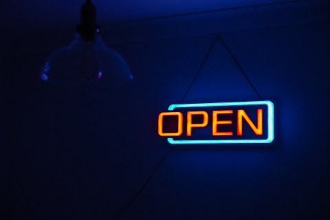 Das Foto zeigt eine Neonleuchttafel, auf der in orangefarbenen Lettern "OPEN" steht. Der Hintergrund ist dunkelblau.