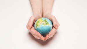 Foto von den Händen einer Person, die die Erde in Form eines Balles mit den Händen umschließt.