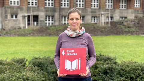 Frau vor dem Fritz-Förster-Bau mit Schild zum SDG 4