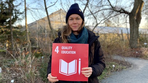 Eine Frau die eine rote Karte mit der weißen Aufschrift 4 Quality Education in den Händen hält. 