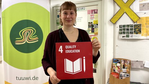 Eine Frau die eine rote Karte mit der weißen Aufschrift 4 Quality Education in den Händen hält.