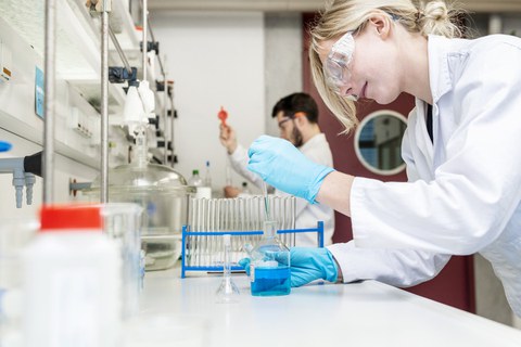 Foto zeigt zwei Studenten, die im Labor arbeiten. Sie tragen Arbeitskleidung und Schutzbrille