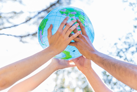 Photo of the hands of two people holding a globe in the air together