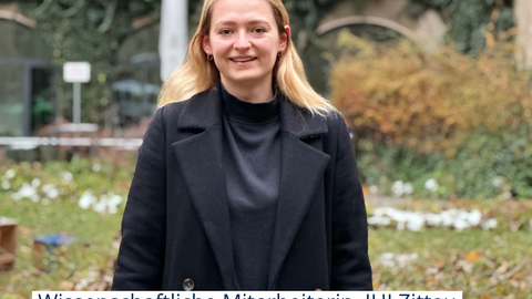 Foto von Lisa Junge, sie steht Hof des Hülsse-Bau auf dem Campus der TUD und lächelt in die Kamera.