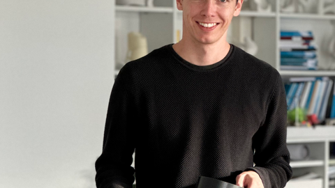 Photo of Nikolas Neumann holding his research materials and smiling at the camera