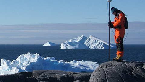 Foto eines Forschenden in der Westantakrtis, der Bodenmessungen vornimmt. Im Hintergrund sind Eisberge zu sehen. 