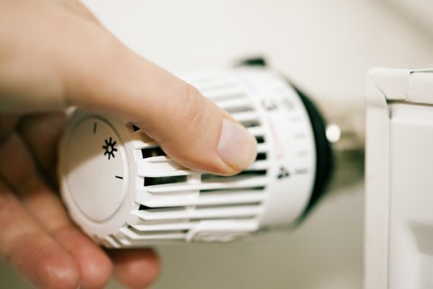Das Foto zeigt eine Hand, die an einem Thermostat einer Heizung dreht.