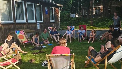 Foto von mehreren Personen, die auf einer Wiese auf Stühlen im Kreis sitzen