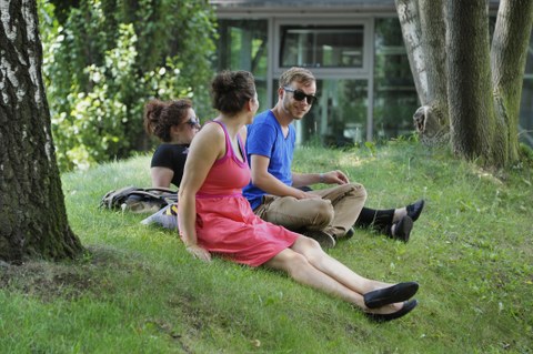 Nahaufnahme von drei Studierenden, die unter einem Baum auf einer Wiese sitzen